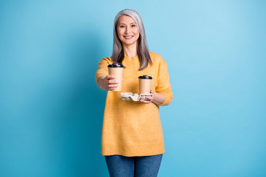 Enjoy your drink. Photo of charming lovely mature courier lady white grey hairdo hold two cup coffee deliver you home wear yellow pullover denim isolated blue pastel color background