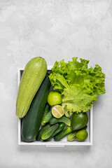 Variety of organic green raw vegetables and fruits: zucchini, cucumber. avacado, apple, lime in a white box on a gray background. Healthy lifestyle. Balanced diet. Green detox
