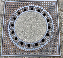 Ein Gullydeckel viereckig auf der Straße.