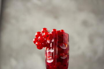 Red currant in a shot glass, the rest is scattered around it on a gray textured background
