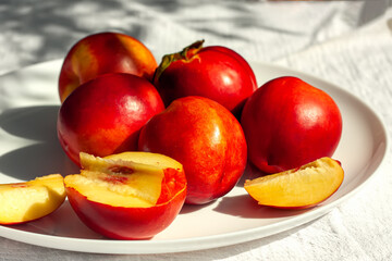 Red ripe organic nectarine fruits on the white plate on nature background. Summertime healthy eating concept. Fruit antioxidant. Selective focus
