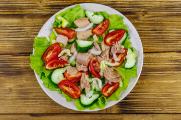 Tasty tuna salad with lettuce and fresh vegetables on wooden table. Top view