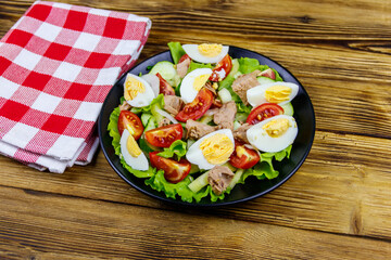 Tasty tuna salad with eggs, lettuce and fresh vegetables on wooden table