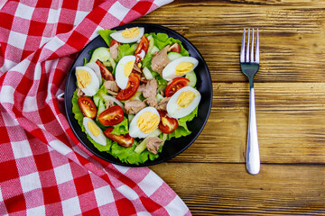 Tasty tuna salad with eggs, lettuce and fresh vegetables on wooden table. Top view