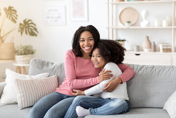 Obraz premium Happy Black Mother Embracing Her Cute Little Daughter On Couch At Home