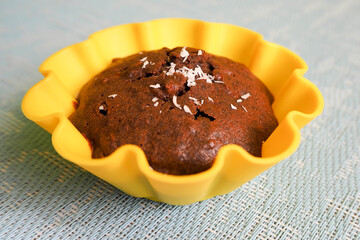 gluten-free chocolate muffin in yellow silicone form on a blue textured background side view . sweets prepared at home