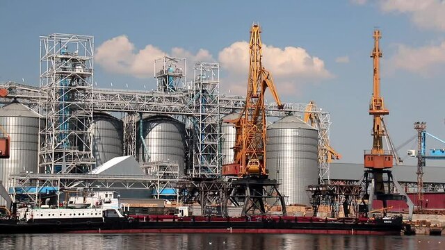 Odesa, Ukraine. Yellow harbor cranes unload a barge at the Odessa International Seaport amid large metal tanks. Big cargo port at sea, delivery, unloading of ships, storage of goods