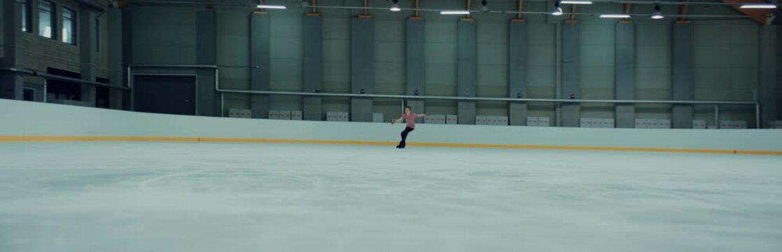Professional teenager male ice figure skater practicing on the indoor rink. Shot on RED cinema camera with 2x Anamorphic lens, 75 FPS slow motion