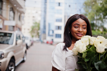 Beautiful african american girl holding bouquet of white roses flowers on dating in the city. Black businesswoman with bunch of flowers near car.