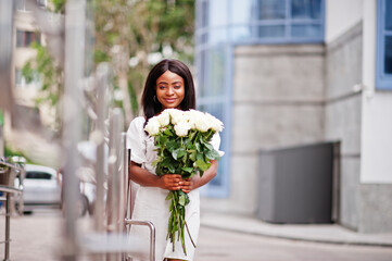 Beautiful african american girl holding bouquet of white roses flowers on dating in the city. Black businesswoman with bunch of flowers.