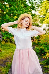 Gorgeous young  woman in hat posing in a blooming garden. Beautiful girl dressed in pink skirt and white blouse. Sensual woman with perfect skin and with natural makeup. fashion and style concept.