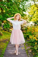 Gorgeous young  woman in hat posing in a blooming garden. Beautiful girl dressed in pink skirt and white blouse. Sensual woman with perfect skin and with natural makeup. fashion and style concept.