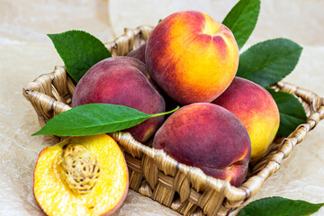 Fresh juicy red, yellow and orange peaches in the wooden basket on light table background in summer season.