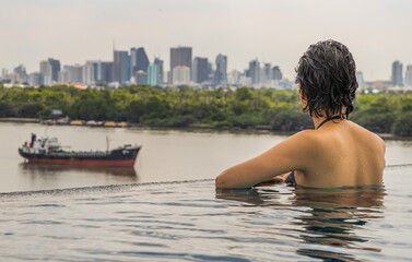Side view of Short haired young woman relax in the roof top outdoor swimming pool and enjoying the city view Bangkok. Summer vacation concept.