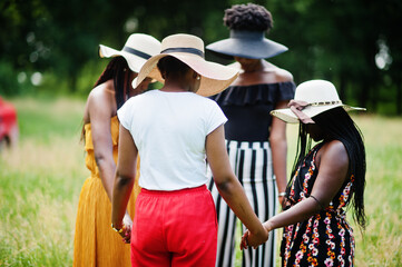 Group of four gorgeous african american womans wear summer hat holding hands and praying at green...