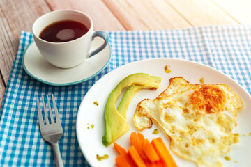 Egg, avocado slices, carrot sticks with a cup of coffee for breakfast
