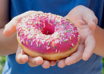 Close-up of children's hands holding a donut with pink icing and sprinkling. Unhealthy food...