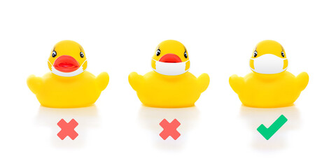 cute yellow rubber ducks in face masks on white background, image shows how to wear mask properly covering over nose and mouth, concept of flu prevention during situation of COVID-19 to stop pandemic