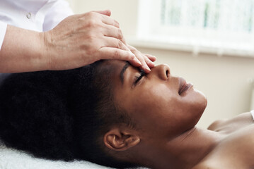 Obraz na płótnie Canvas A young black woman lies in the beautician's office and relaxes from gentle touches and toning massage. The concept of spa treatments