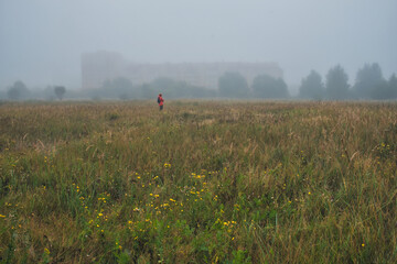 Fog-covered fields, cool morning, fog, withered grass, house in the fog, a man in a red jacket