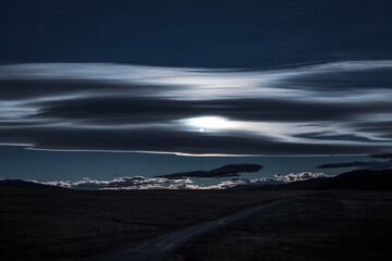 Sunset with the sun behind clouds landscape. Faint dark image of straight road leading to the mountains of patagonia. Image similar to night and moon.