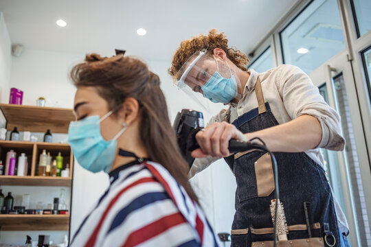 Woman wearing face mask getting fresh styling at a hairdresser shop. Adult woman at hairdresser wearing protective mask due to coronavirus pandemic. A hairdresser with security measures for Covid-19