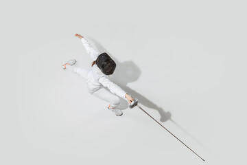 Attacking. Teen girl in fencing costume with sword in hand on white background. Top view. Young...