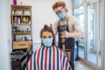 Woman have hair cutting at hair stylist during pandemic isolation, they both wear protective equipment. Hairdresser and customer in a salon with medical masks during virus pandemic. 