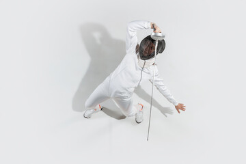 Attacking. Teen girl in fencing costume with sword in hand on white background. Top view. Young...