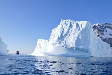 Cruise ship between icebergs in antarctic ocean, blue sky, sun, Antarctica