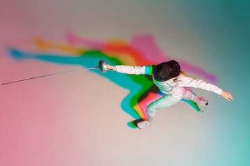 Emotion. Teen girl in fencing costume with sword in hand on gradient background in neon light. Top...