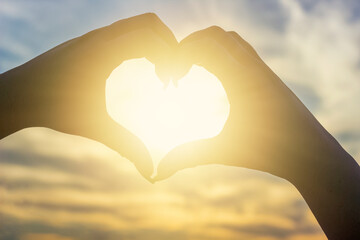 fingers folded in a heart on a sunset background