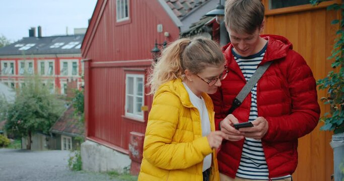 Couple of young tourists in centre of old European town or city. Look at map or city guide on smartphone application. Happy staycation and exploring. Modern millennial conscious tourism generation