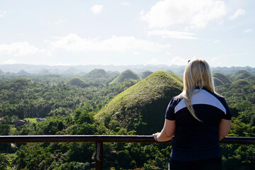 Fototapeta na wymiar Blonde woman at view point in Bohol looking at the inspirational view of the chocolate hills and mountains. This picturesque landscape is a famous tourist attraction in the Philippines.