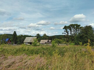 Obraz premium houses of a small village among green grass and trees against a blue cloudy sky on a sunny day
