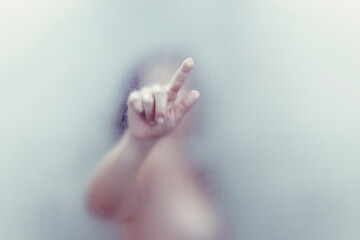 Naked beautiful woman taking a shower and touches hand wet misted glass.