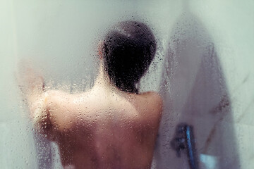 Naked beautiful woman taking a shower behind wet misted glass.