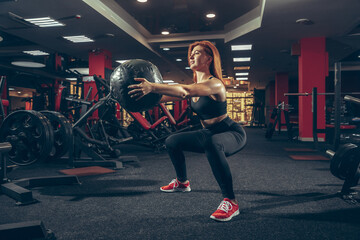 Fototapeta na wymiar Strong. Young muscular caucasian woman practicing in gym with equipment. Athletic female model doing exercises, training her lower body, working out with ball. Wellness, healthy lifestyle