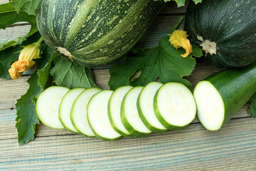 fresh green zucchini or marrow with slices with flowers and leaves on wooden background. Top view