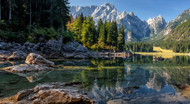 Impressive Autumn landscape during sunrise. The Fusine Lake in front of the Mongart under sunlight. Amazing sunny day on the mountain lake. concept of an ideal resting place. Creative image.