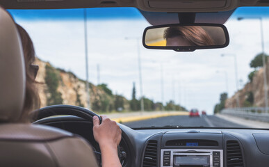 The girl is driving on the highway in Spain. View from the back seat of the car on the windshield, road and the driver