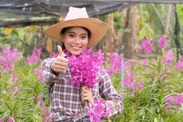 Foto op Canvas A woman gardener wearing a plaid shirt wearing a hat is holding a pink orchid in his hand. And was smiling happily. In the orchid garden © Prot