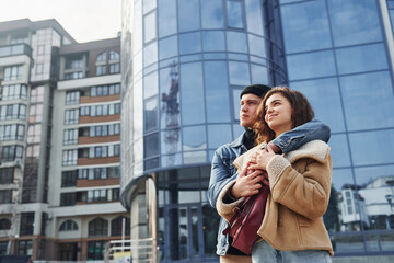 Fototapeta premium Cheerful couple in casual warm clothes have a walk outdoors in the city near business building