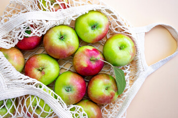 Ripe juicy apples in a mesh eco bag on a beige background. View from above.