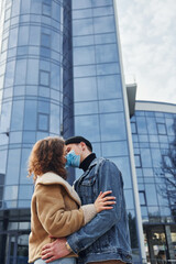 Fototapeta premium Couple in protective masks kissing each other in the city near business building at quarantine time. Conception of coronavirus