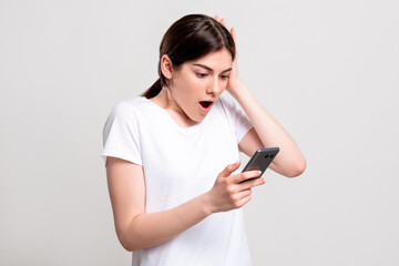 Fototapeta premium Surprised woman portrait. Special offer. Amazed lady reading message with good news on smartphone isolated on neutral background. Exciting opportunity. Wow reaction.
