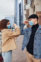 Couple in protective masks greeting each other in the city near business building at quarantine time. Conception of coronavirus