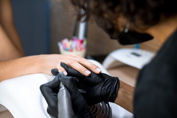 manicurist master in black gloves and mask is making manicure with a manicure drill apparatus in the spa salon