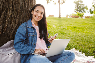 Image of joyful asian student woman using laptop and mobile phone