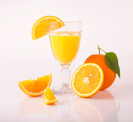 Glass of orange juice and orange sections on white background.